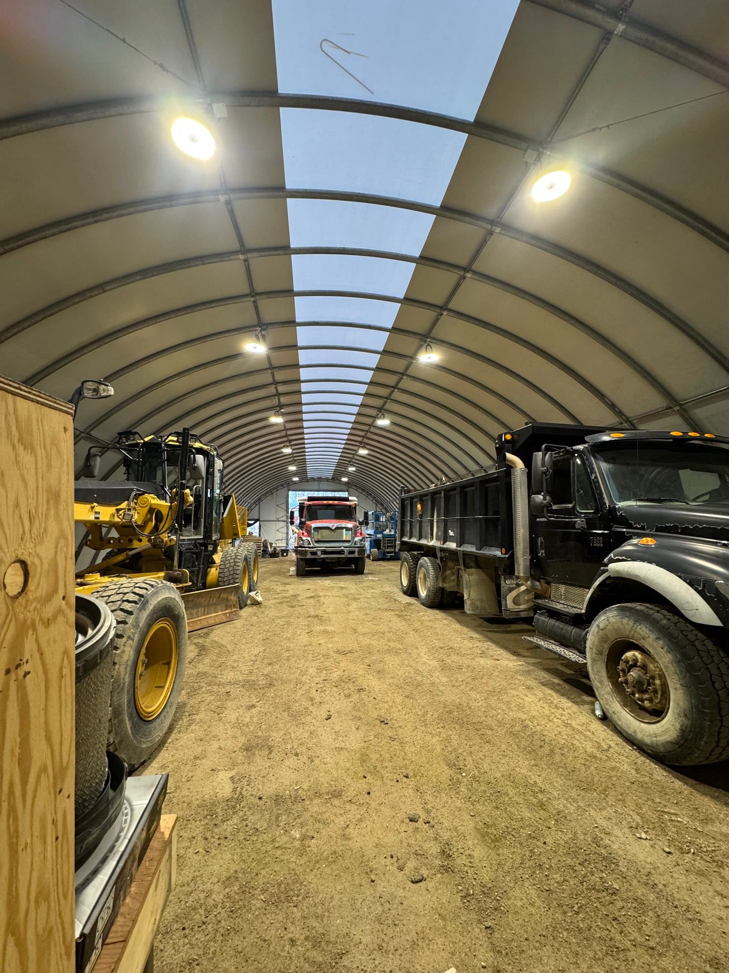 The lit interior of a fabric arch building with trucks and a loader parked inside.