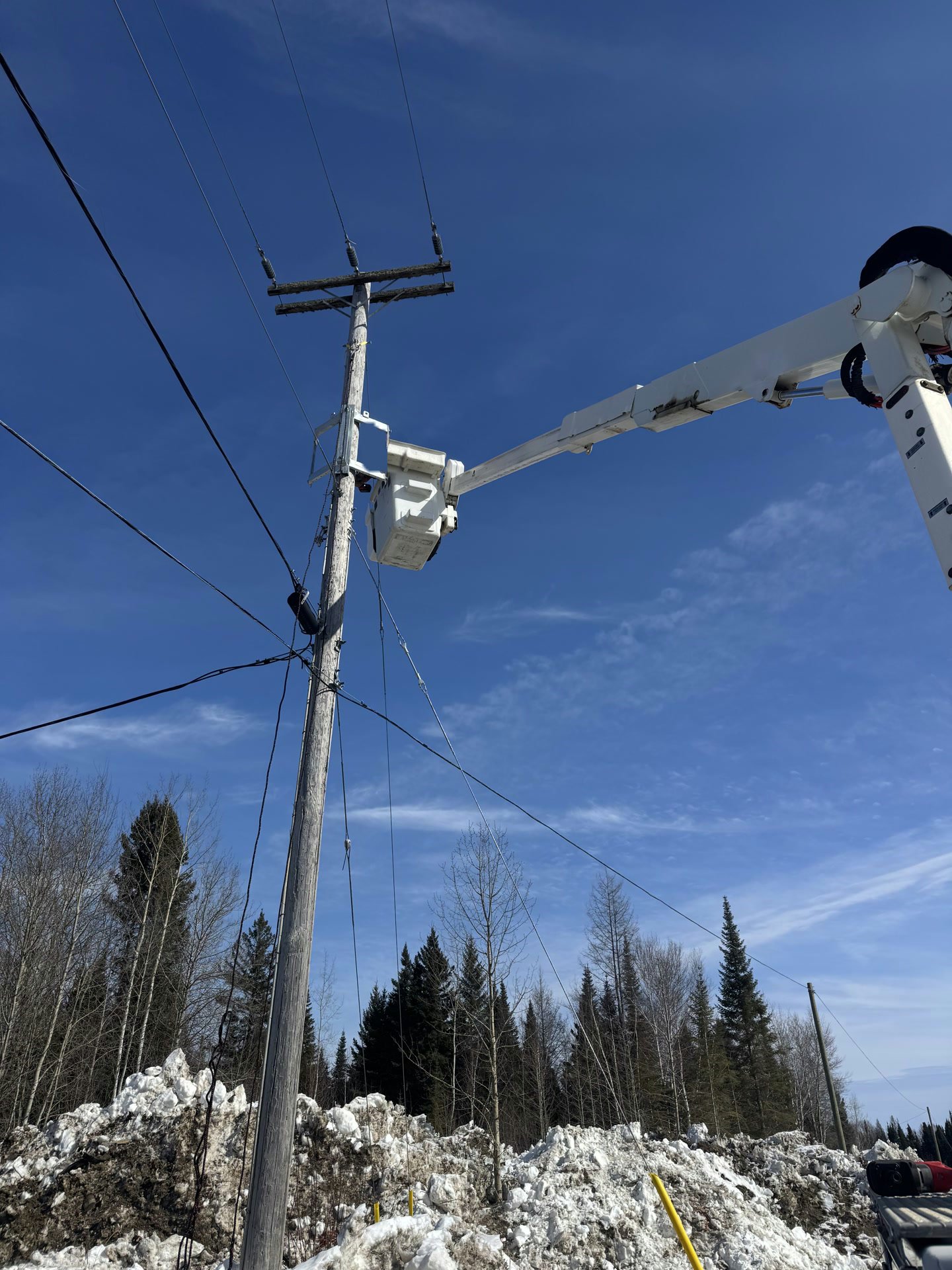 A bucket truck boom working at the top of a power pole against a deep blue sky.